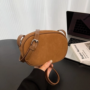 Minimalist brown suede oval crossbody bag with adjustable strap and silver buckle