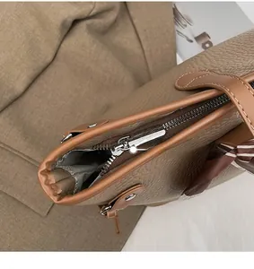 Detail eines glatten Metallreißverschlusses und Seidenschals an brauner Leder-Tragetasche