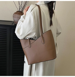 Sac fourre-tout marron en cuir grainé porté avec un manteau beige dans un décor d'intérieur épuré