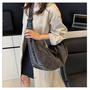 Detail of a large dark grey washed denim crossbody bag with adjustable buckle strap