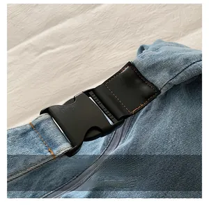 Detail of the durable plastic buckle and brown stitching on a light blue denim bag