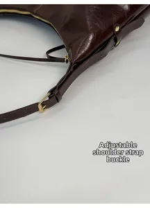 Detail of dark brown leather shoulder strap with adjustable golden buckle closure