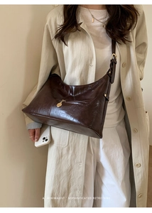 Detail of dark brown retro leather hobo bag with gold charm on beige trench coat
