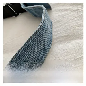 Close-up of a wide denim shoulder strap with brown contrast stitching and buckle detail