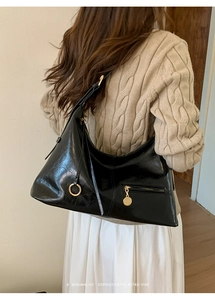 Detail of glossy black hobo bag showing oily leather texture and golden zipper hardware