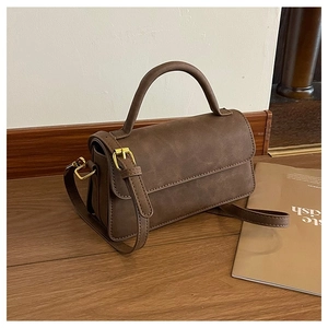 Sac bandoulière rétro marron en cuir avec boucle dorée sur sol en bois