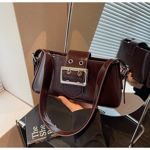 Close-up of glossy chocolate brown shoulder bag with a large silver buckle and belt detail