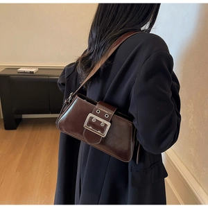 Detail of a dark brown square crossbody bag featuring a large silver buckle and glossy finish
