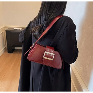 Detail view of burgundy leather underarm bag with large silver buckle on black coat