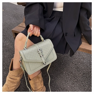 Détail d'un sac à main tressé vert sauge avec boucle argentée tenu par un mannequin