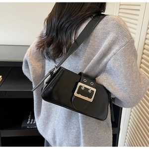Detail of a shiny black leather shoulder bag with a large silver buckle on a model