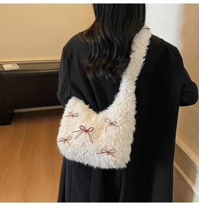 Plush shoulder bag with red bows and gold bells shown on model wearing black coat
