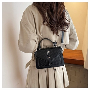Détail d'un sac à bandoulière matelassé noir porté avec un trench beige pour un look chic
