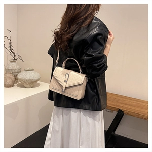 Détail d'un sac à bandoulière matelassé beige avec boucle en métal porté par un mannequin chic