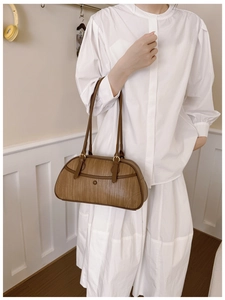 Detail of a brown woven texture retro shoulder bag with twin handles on a white outfit