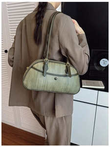 Détail d'un sac bandoulière tissé vert foncé avec des finitions dorées sur modèle
