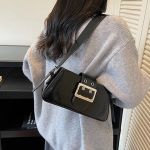 Minimalist black patent leather baguette bag with silver buckle and wide strap on shoulder