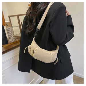 Detail of beige nylon crescent crossbody bag featuring multi-pocket utility and wide strap