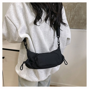 Detail of a puffy black nylon crossbody bag with side drawstring and adjustable strap