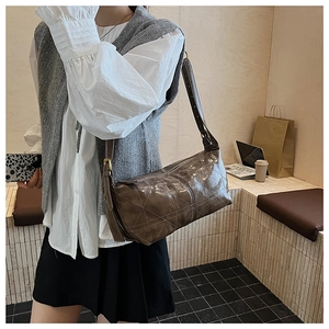 Detail of dark brown glossy shoulder bag with large diamond stitching and wide strap