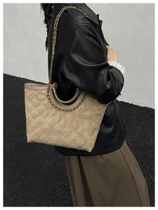 Close-up of beige quilted tote bag with gold chain strap on a model wearing leather