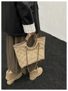 Détail d'un sac cabas matelassé beige avec chaîne dorée porté par un mannequin