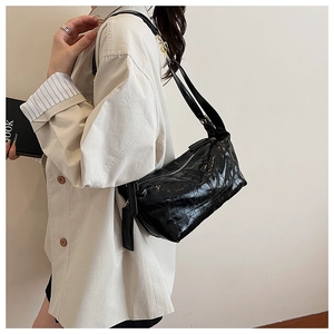 Detail of glossy black quilted dumpling bag worn over shoulder with casual office outfit