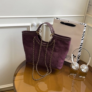 Borsa tote trapuntata viola scuro con tracolla a catena e manici su tavolo