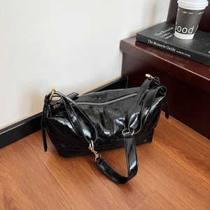 Quilted glossy black patent leather shoulder bag with golden hardware on a wooden floor