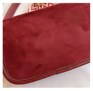 Makroaufnahme einer burgunderroten Mattledertasche mit rot-weißem gewebtem Schultergurt