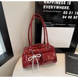 Détail du sac en cuir verni bordeaux avec breloque nœud en perles sur un bureau chic