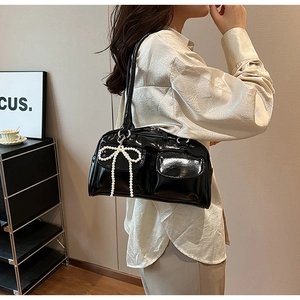 Détail du sac sous le bras en cuir verni noir avec doubles poches et breloque noeud en perles