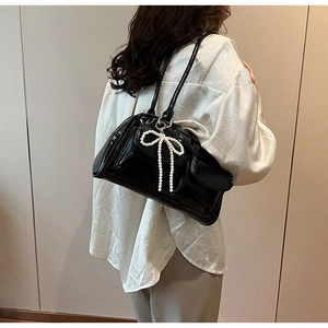 Détail du sac Boston en cuir verni noir avec charm nœud décoratif en perles blanches