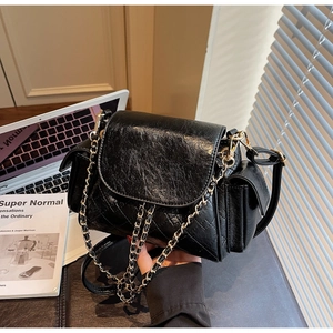 Detail of black quilted shoulder bag with chain strap and glossy leather texture