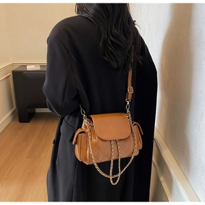 Brown quilted crossbody bag with metal chain strap worn by model in a minimalist setting