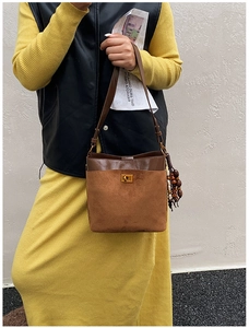 Detail of brown leather bucket bag with gold metal lock and beaded wood tassel charm