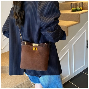 Detailed view of brown suede bucket bag with gold clasp shown in a lifestyle setting