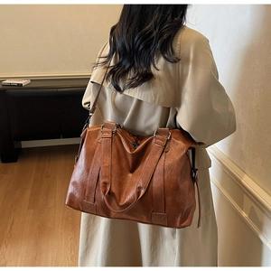 Detail of vintage brown leather pillow bag showing the wide strap and texture on a model