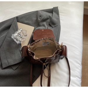 Detail of dark brown quilted backpack with gold chain straps and drawstring closure