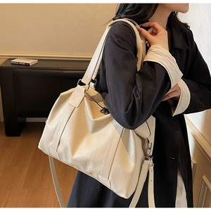 Detail of a cream-colored leather travel tote with wide strap shown on a model