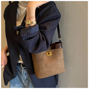 Detail view of brown suede bucket bag with gold clasp shown with a striped blazer