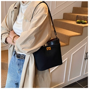 Detail of black crossbody bag with gold lock buckle shown on model in stair setting