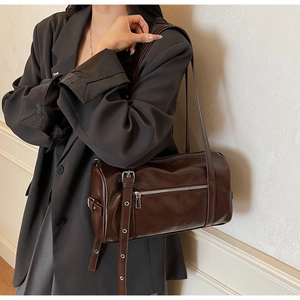 Detail of dark brown leather cylinder bag with silver hardware on grey blazer