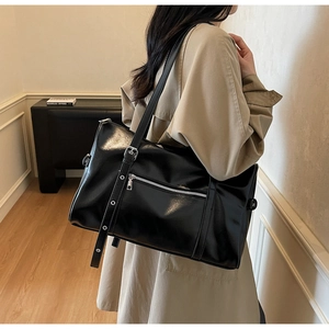 Close-up of shiny black faux leather shoulder bag with silver zipper and side buckle detail