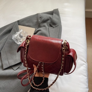 Quilted burgundy crossbody bag with gold chain strap on grey blazer background
