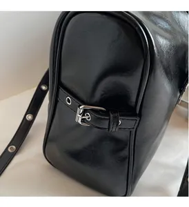 Detailed macro view of black glossy leather bag with silver metal buckle and adjustable strap