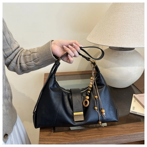 Detail of black pebbled leather handbag with gold metal clasp and wooden bead charm