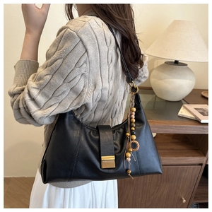 Detail of black leather bag featuring a gold metal buckle and unique wooden bead charm