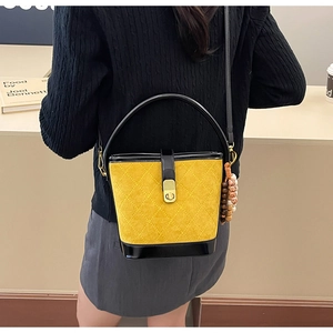 Détail du sac seau en daim jaune matelassé avec poignée en cuir verni noir et breloque