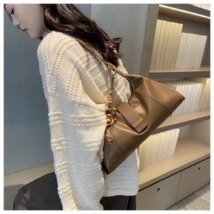 Detail of a brown leather hobo bag with a beaded tassel charm on a model